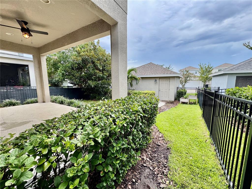 A covered patio overlooks a backyard with a manicured hedge, grass, and a detached shed — 7208 MILESTONE DRIVE, APOLLO BEACH, FL