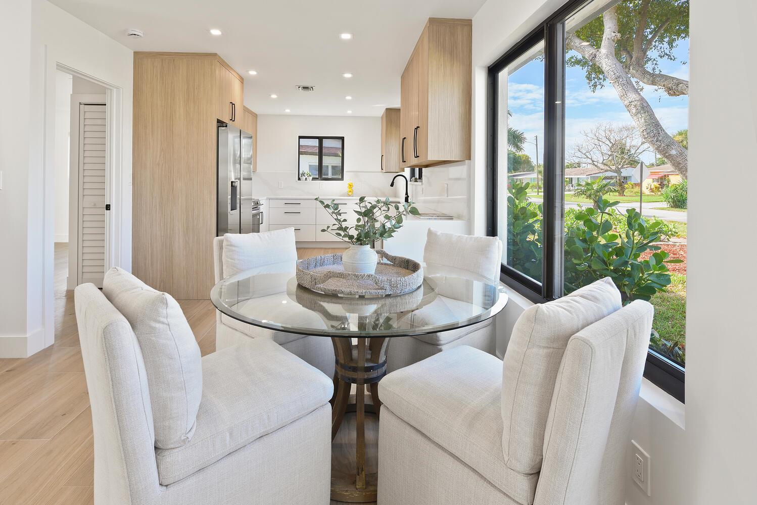 A dining area with a glass table and four chairs sits before a modern kitchen — 1320 S Deerfield Avenue, Deerfield Beach FL 33441, DEERFIELD BEACH, FL