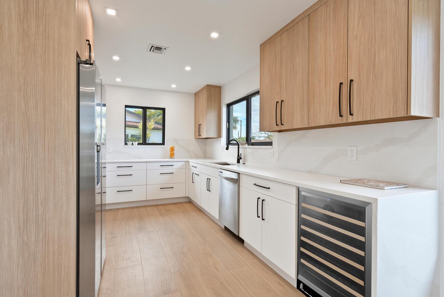 A modern kitchen features light wood cabinetry, white countertops, stainless steel appliances, and wood flooring — 1320 S Deerfield Avenue, Deerfield Beach FL 33441, DEERFIELD BEACH, FL