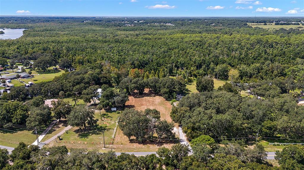 An aerial view shows a cleared, grassy lot surrounded by dense trees and nearby houses — LAKE UNITY ROAD, FRUITLAND PARK, FL