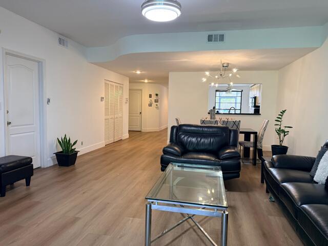 A living room features light wood flooring, black leather furniture, and an open dining area — 8659 Vía Reale # 1, Boca Raton FL 33496, BOCA RATON, FL
