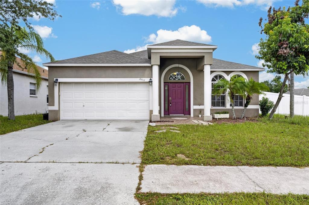 A single-story house with a white garage door, a purple front door, and two columns — 24519 BREEZY OAK COURT, LUTZ, FL