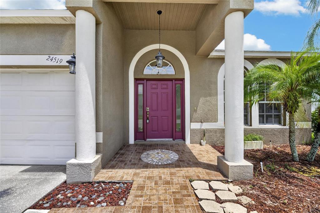The exterior of a house features a purple front door, white columns, and tiled entryway — 24519 BREEZY OAK COURT, LUTZ, FL