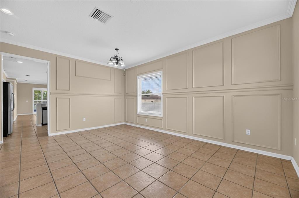 A dining room with tan walls, wainscoting, a chandelier, and light brown tile flooring — 24519 BREEZY OAK COURT, LUTZ, FL
