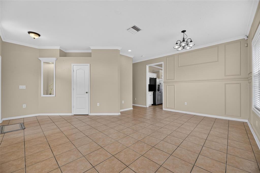 A spacious room with beige walls, tile flooring, a chandelier, and a white interior door — 24519 BREEZY OAK COURT, LUTZ, FL