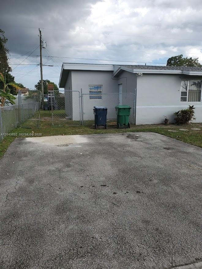 A gray house exterior features a paved driveway, a chain-link fence, and two trash bins — 14721 SW 104th Ave, Miami FL 33176, MIAMI, FL