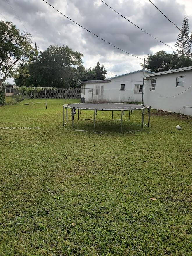 A backyard features a large trampoline on a grassy lawn next to a white house — 14721 SW 104th Ave, Miami FL 33176, MIAMI, FL