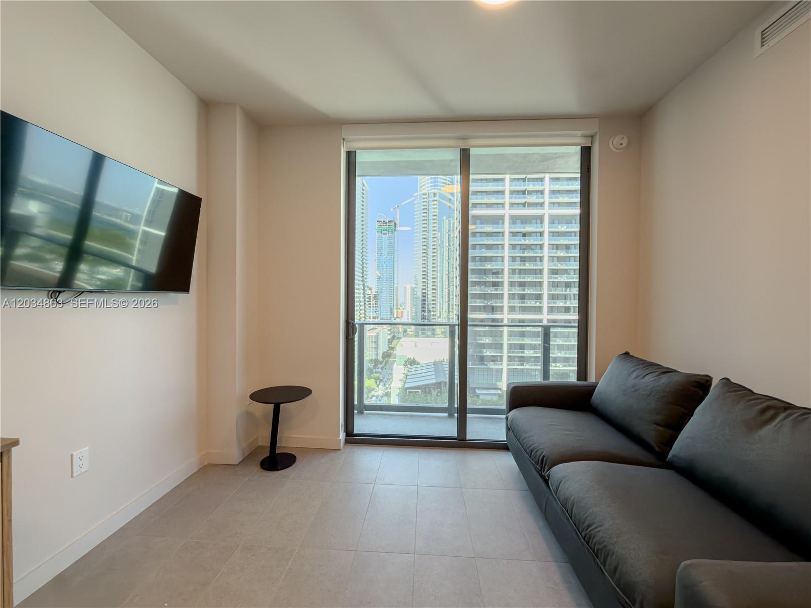 A living room features a dark sofa, a wall-mounted television, and a sliding glass door — 121 NE 5th St # 2211, Miami FL 33132, MIAMI, FL