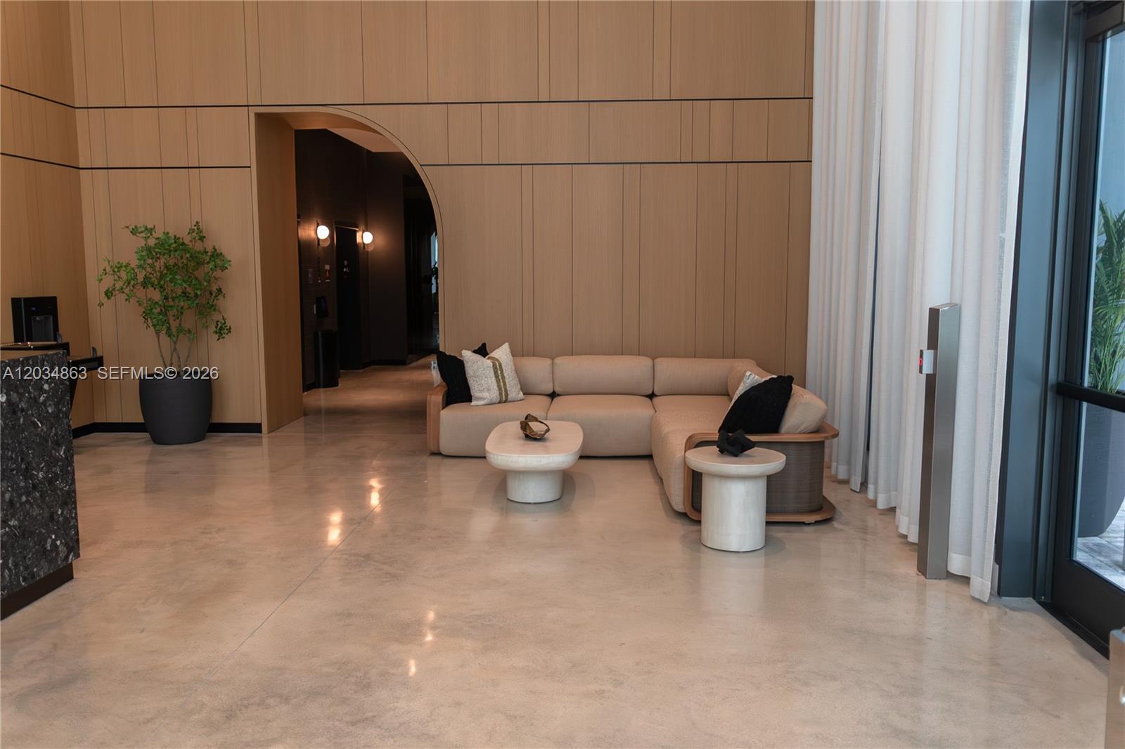 A modern lobby features a beige sectional sofa, stone coffee tables, and wood-paneled walls — 121 NE 5th St # 2211, Miami FL 33132, MIAMI, FL