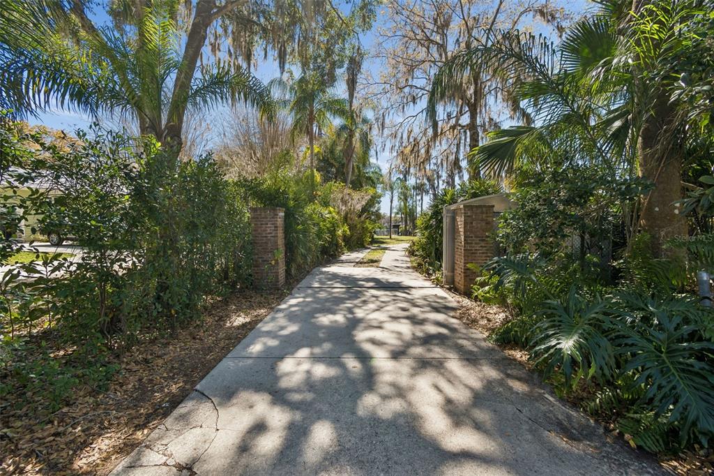 A concrete driveway leads through brick pillars into a lush, tree-lined yard — 16515 LAKE CHURCH DRIVE, ODESSA, FL