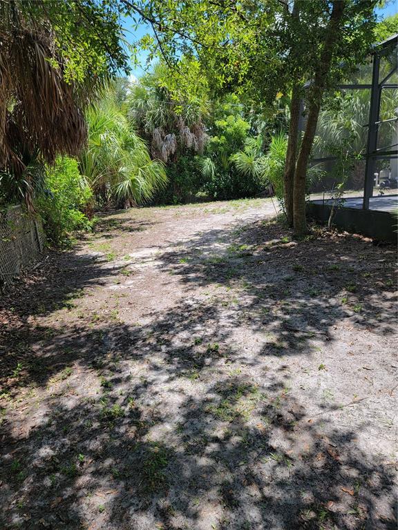 A sandy backyard area with sparse vegetation, trees, and a screened-in pool enclosure — 5990 GILLOT BOULEVARD, PORT CHARLOTTE, FL