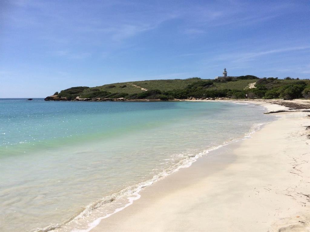 A sandy beach stretches toward a grassy headland topped by a lighthouse under a blue sky — PR-301 CONDO. VISTAMAR EL COMBATE UNIT B-207, CABO ROJO, PR