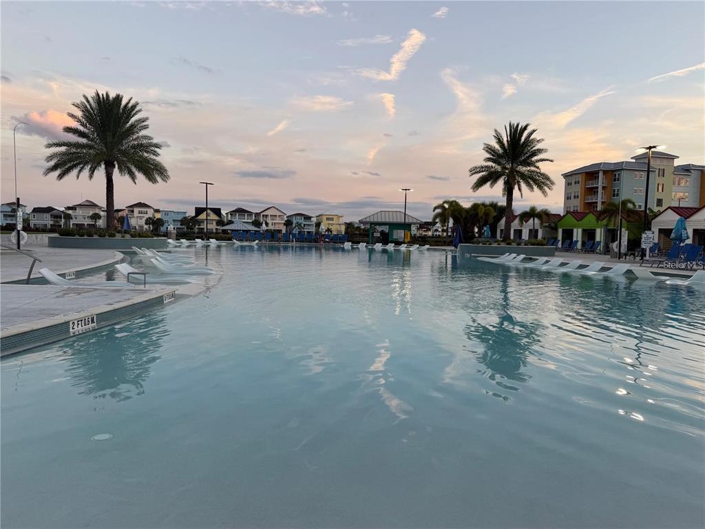 A large resort-style swimming pool features lounge chairs in the water under a sunset sky — 8061 VACATION AVENUE UNIT 216, KISSIMMEE, FL