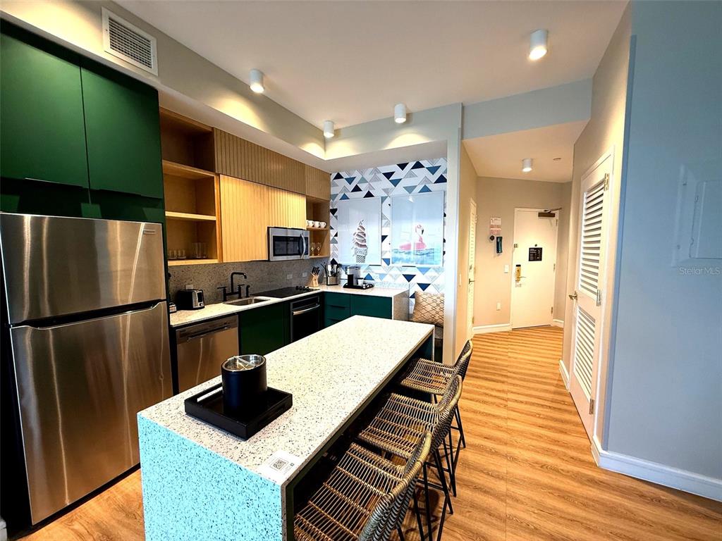 A kitchen features green cabinets, a speckled island with bar stools, and geometric wall art — 8061 VACATION AVENUE UNIT 216, KISSIMMEE, FL