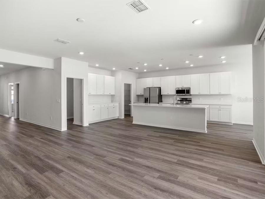 A modern kitchen features white cabinetry, a large island, and light wood-look flooring — 8679 WILDFLOWER FIELD LANE, WILDWOOD, FL