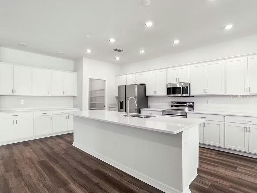 A modern kitchen features white cabinetry, a large central island, and dark wood-look flooring — 8679 WILDFLOWER FIELD LANE, WILDWOOD, FL