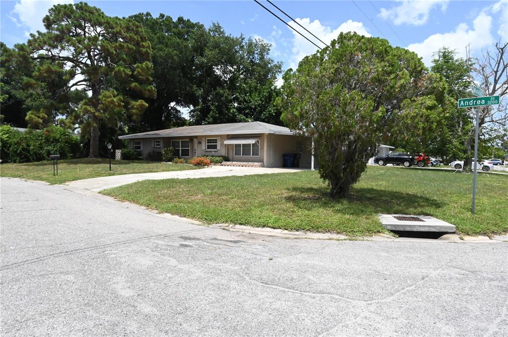 A single-story house with a concrete driveway sits on a corner lot with trees — 3341 ANDREA STREET, SARASOTA, FL
