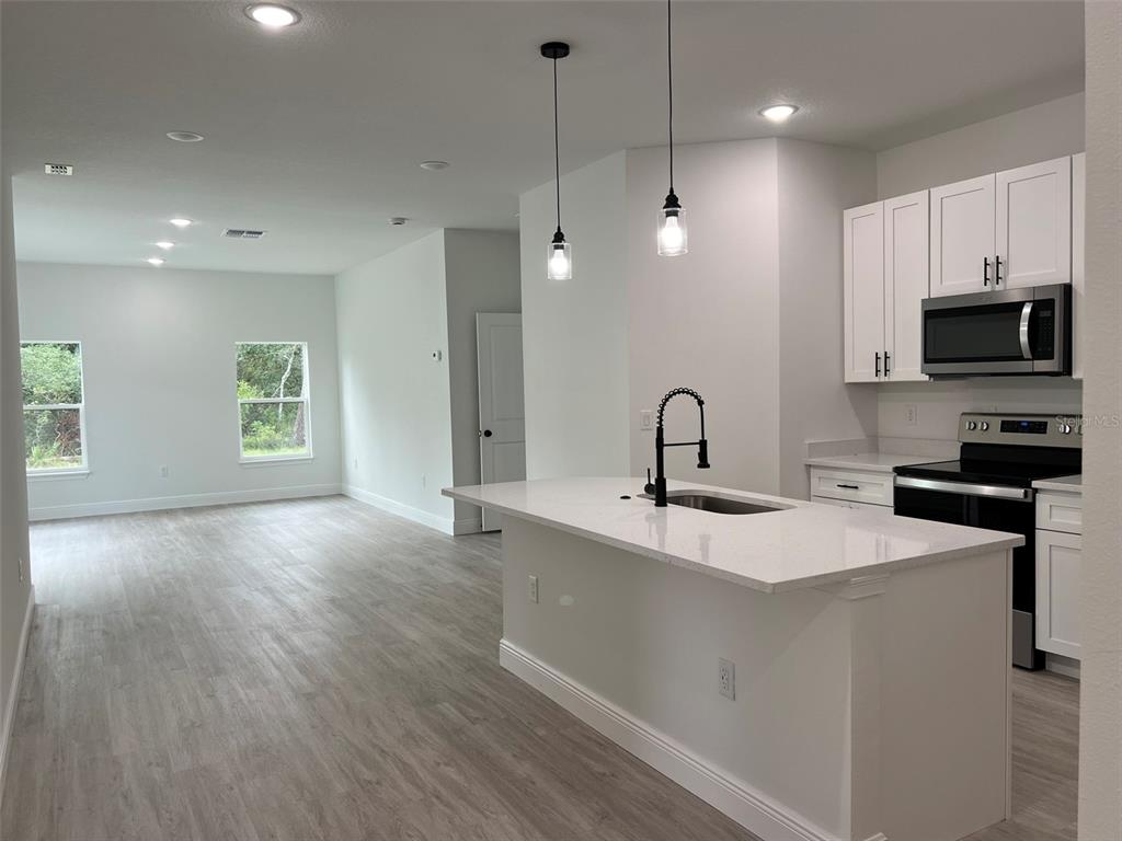 A kitchen with white cabinets and a quartz island overlooks an open living area — 3 FISHER PLACE DRIVE, OCKLAWAHA, FL