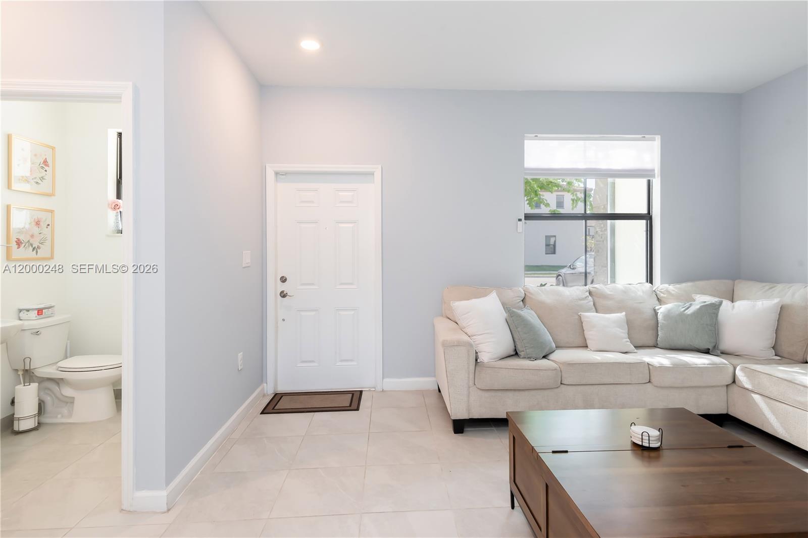 A living room with light blue walls, tile floors, a sectional sofa, and an adjacent bathroom — 23129 SW 99th Ave, Cutler Bay FL 33190, CUTLER BAY, FL