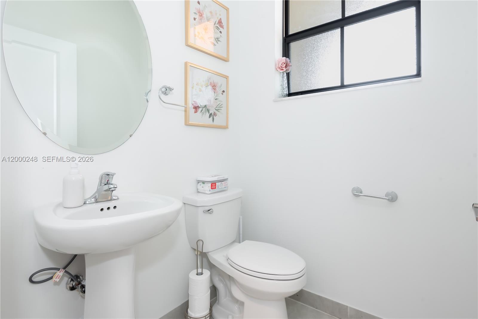 A small bathroom features a pedestal sink, a white toilet, and two floral wall prints — 23129 SW 99th Ave, Cutler Bay FL 33190, CUTLER BAY, FL