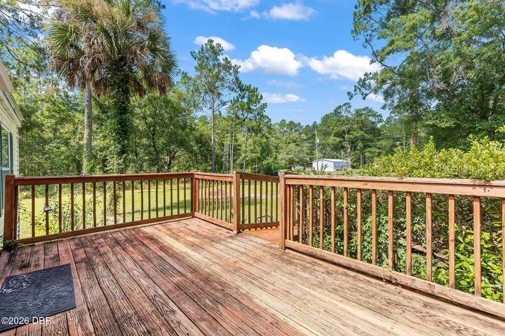A wooden deck with railings overlooks a grassy backyard surrounded by trees — 10120 OLIVER AVENUE, HASTINGS, FL
