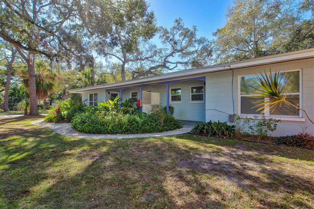 A light blue single-story house features a covered porch and surrounding landscaping under large trees — 1751 6TH STREET, SARASOTA, FL