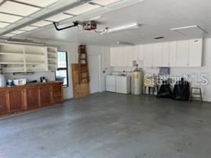 A garage features a concrete floor, wooden cabinets, white wall-mounted storage, and laundry appliances — 2066 KATIE COURT, WINTER HAVEN, FL
