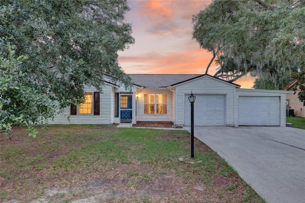 A single-story house with white siding, a two-car garage, and a concrete driveway at dusk — 303 OAK TRACK PASS, OCALA, FL
