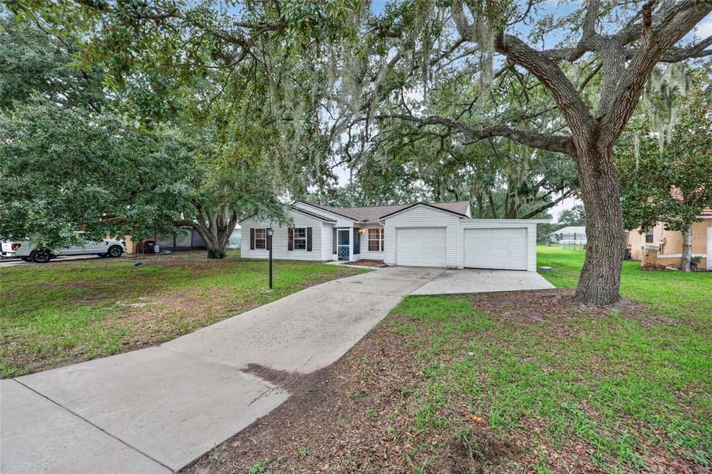 A single-story house with a two-car garage and a concrete driveway under large oak trees — 303 OAK TRACK PASS, OCALA, FL