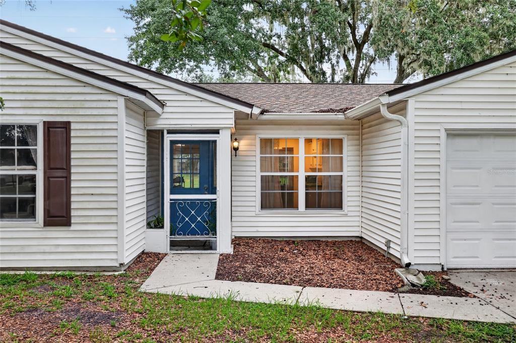 The exterior of a single-story house features white siding, a blue screen door, and a garage — 303 OAK TRACK PASS, OCALA, FL