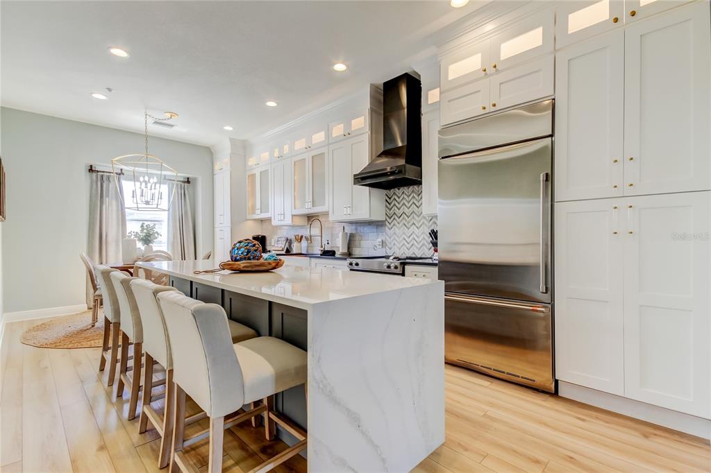 A modern kitchen features white cabinetry, a marble-topped island with bar seating, and stainless appliances — 120 BRIGHTWATER DRIVE UNIT 5, CLEARWATER, FL