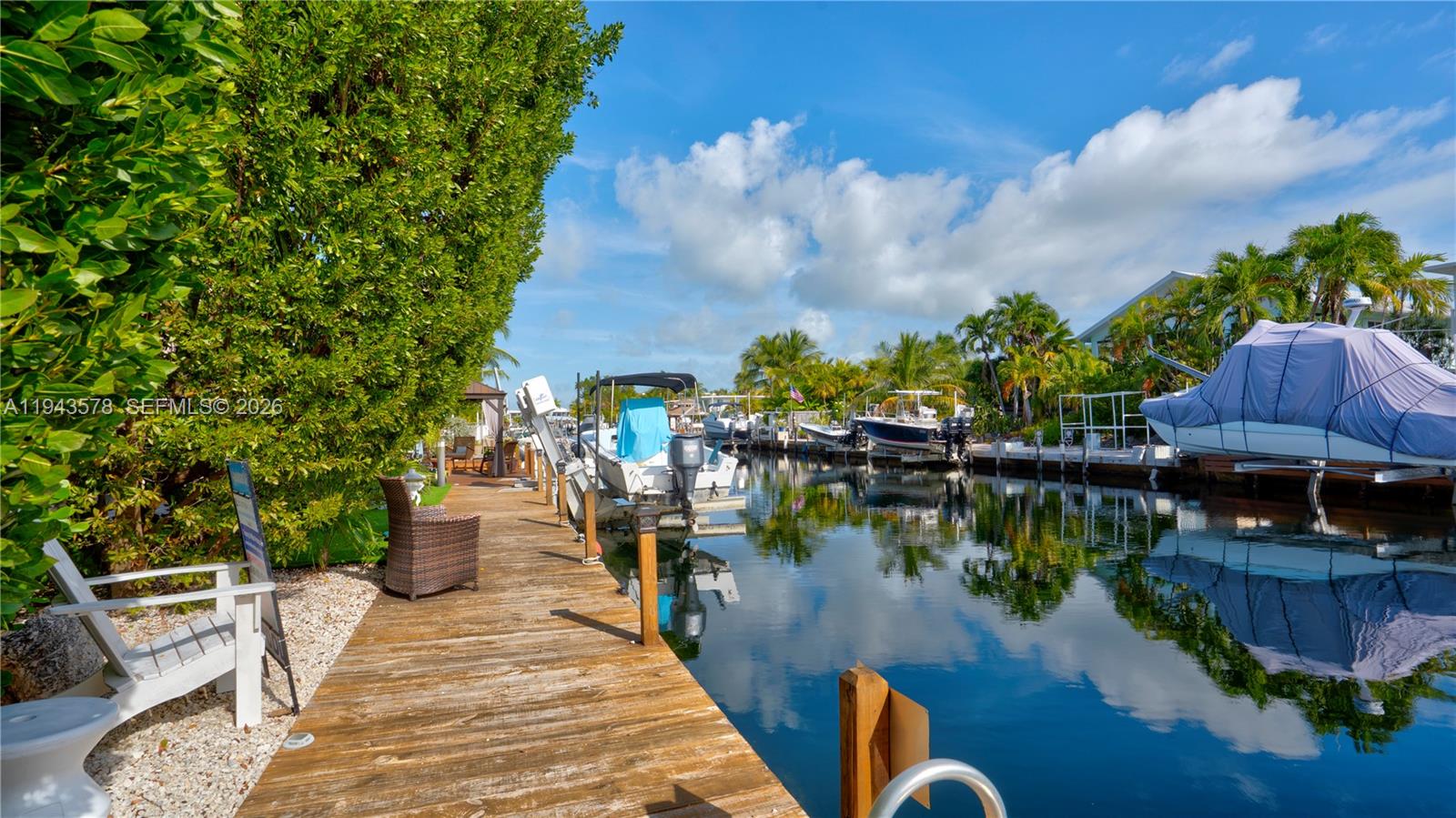 A wooden dock extends along a canal lined with boats and lush tropical vegetation — 150 Azalea St., Plantation Key FL 33070, PLANTATION KEY, FL