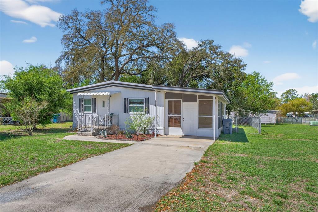 A single-story manufactured home with a concrete driveway, a small front porch, and large trees — 7489 WESTERN CIRCLE DRIVE, BROOKSVILLE, FL