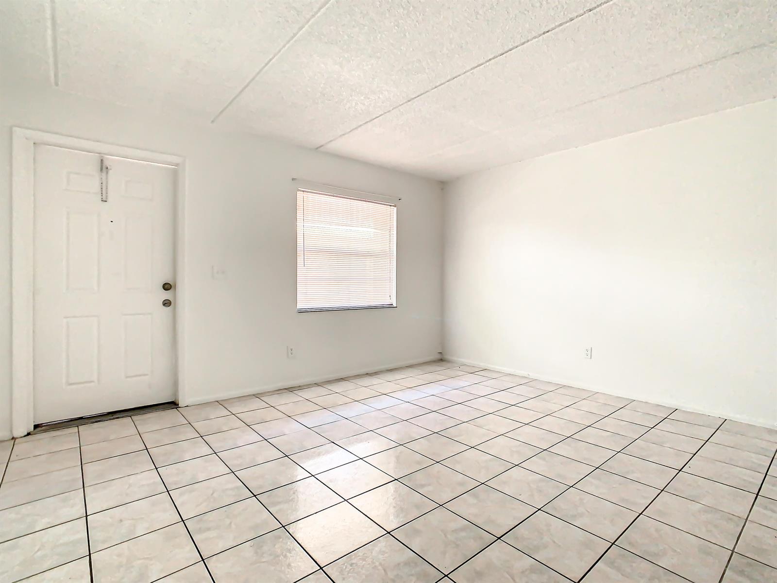An empty room features white walls, a white door, a window with blinds, and tiled flooring — 714 Michigan Court # 4, FL 34769, FL
