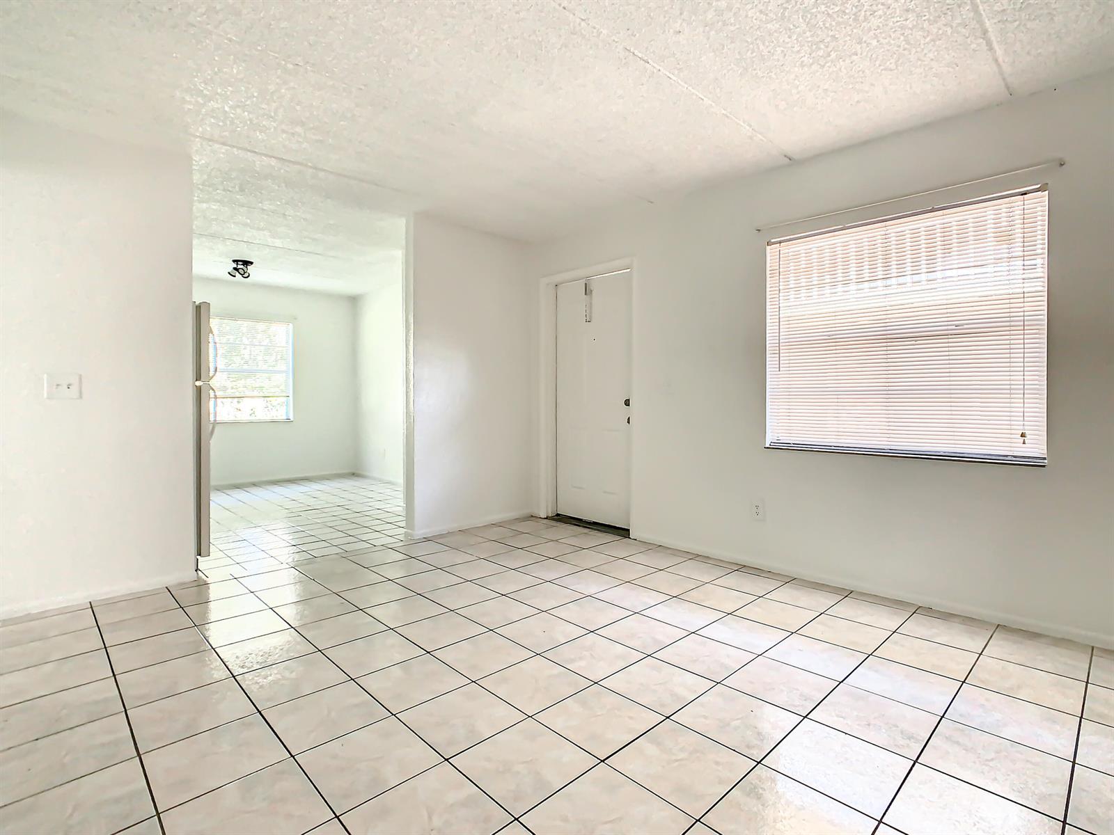An empty room with white walls, tile flooring, a window with blinds, and a doorway — 714 Michigan Court # 4, FL 34769, FL