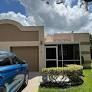 A tan single-story house features a garage, a screened-in entryway, and a landscaped front yard — 9005 Flynn Circle # 1, Boca Raton FL 33496, BOCA RATON, FL