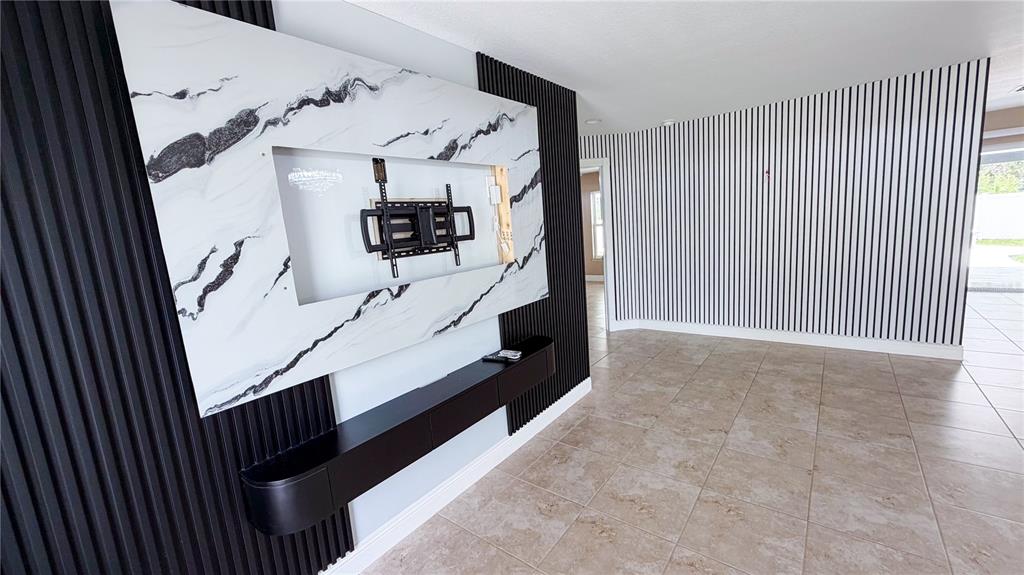 A living room features a marble-look television wall with black vertical slats and tile flooring — 521 MARION OAKS BOULEVARD, OCALA, FL