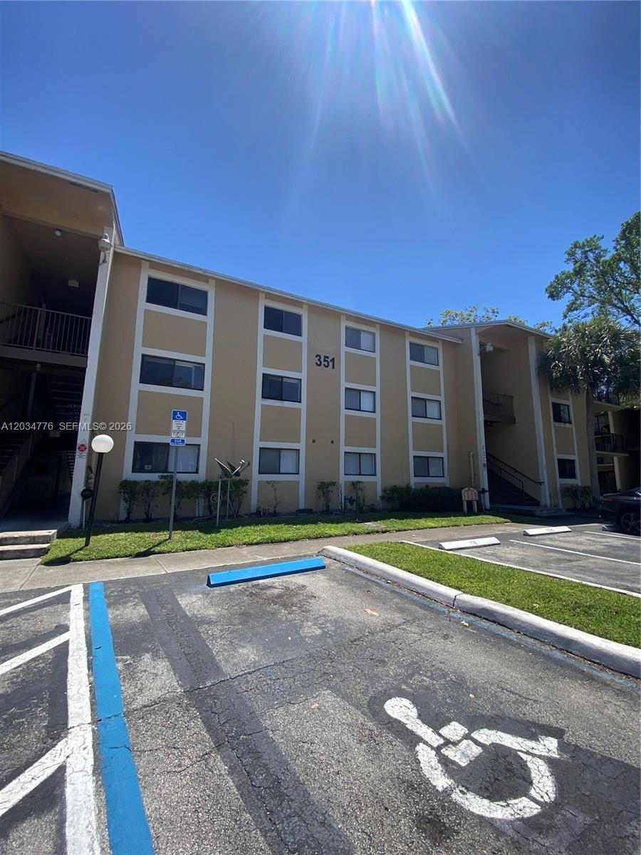 A three-story apartment building exterior features tan stucco walls and a designated handicap parking space — PEMBROKE PINES, FL