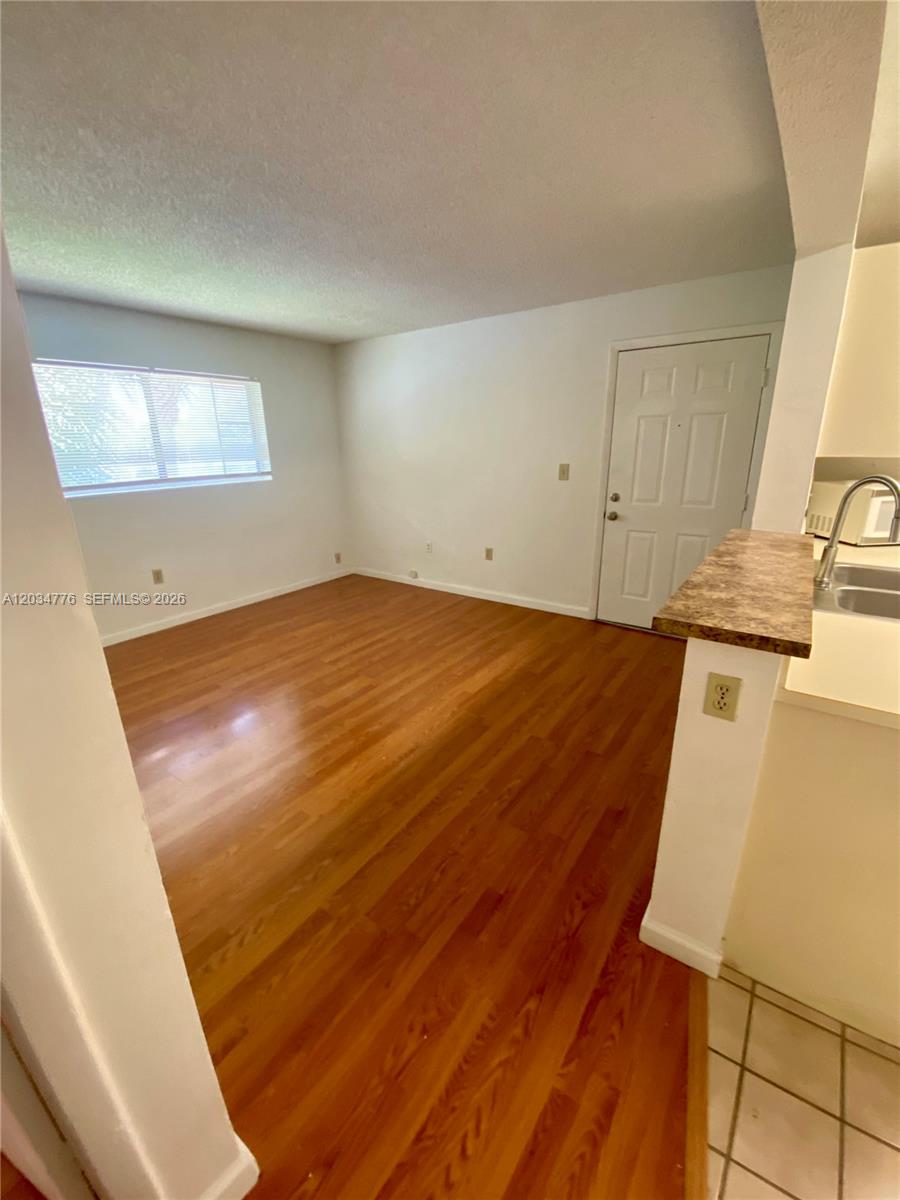 An empty room features wood-look flooring, white walls, a window, and a door — PEMBROKE PINES, FL