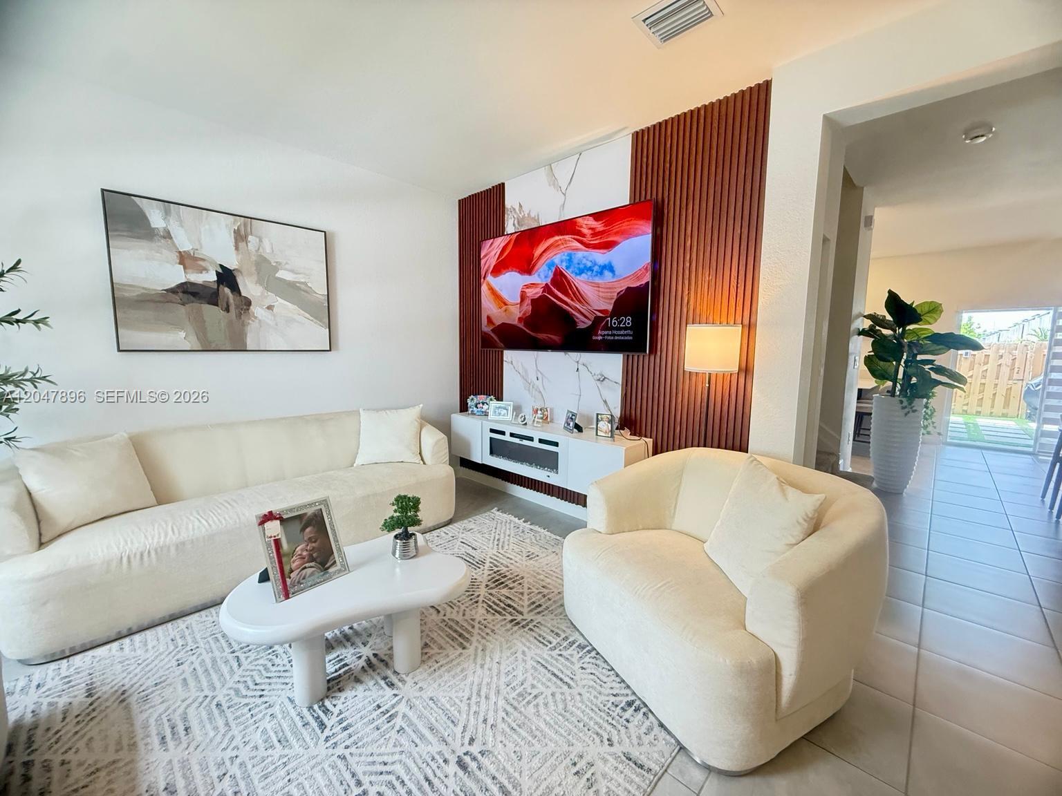 A living room features a white sofa, armchair, patterned rug, and a wood-slatted accent wall — HOMESTEAD, FL
