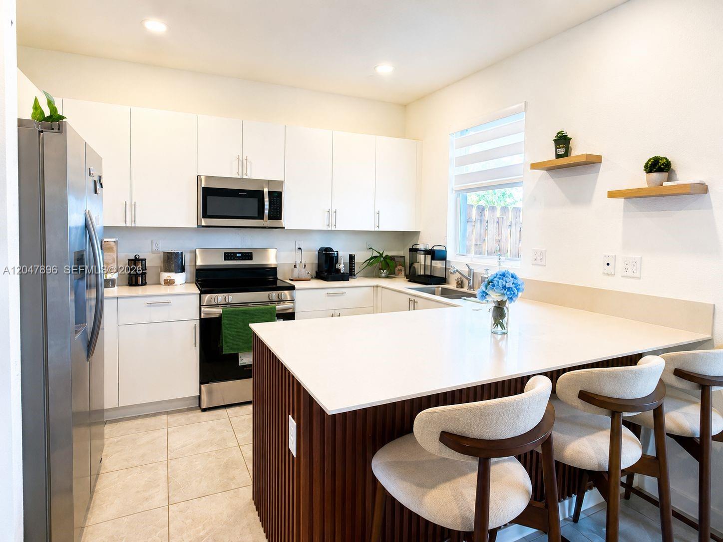 A modern kitchen features white cabinetry, stainless steel appliances, and a slatted wood kitchen island — HOMESTEAD, FL