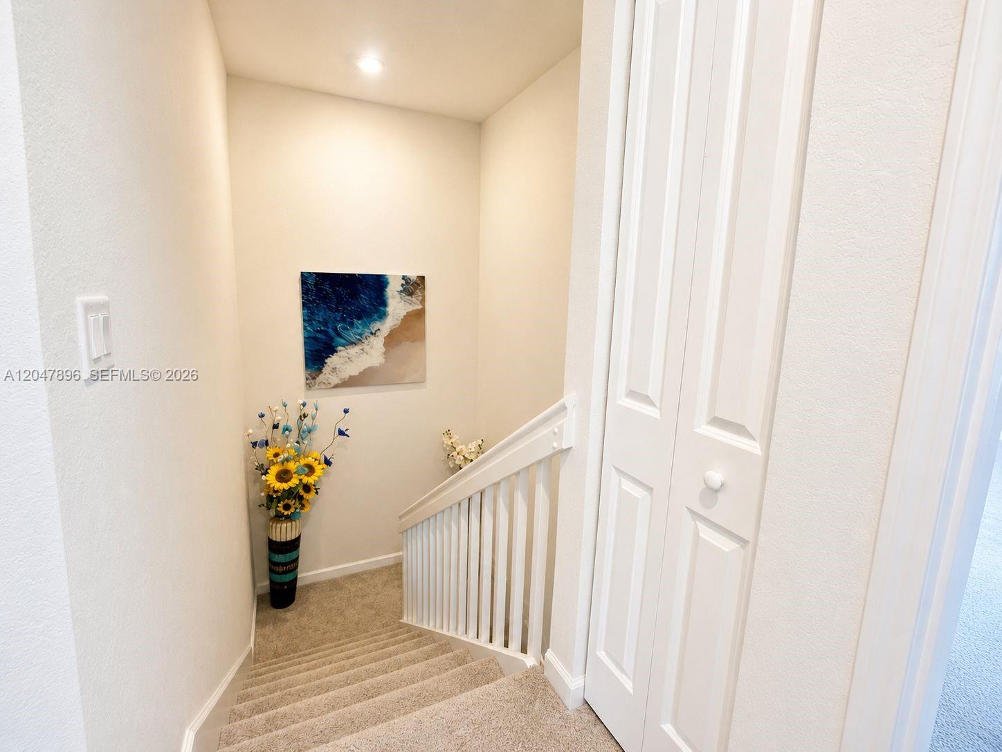 A carpeted staircase leads down to a landing with a painting and floral decor — HOMESTEAD, FL