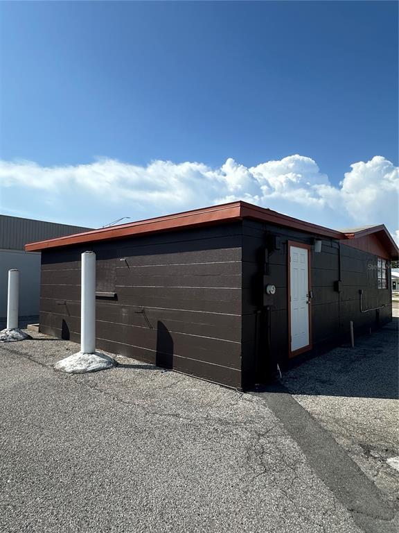The exterior of a dark brown, single-story building with a white door and two bollards — 2254 S TAMIAMI TRAIL, VENICE, FL