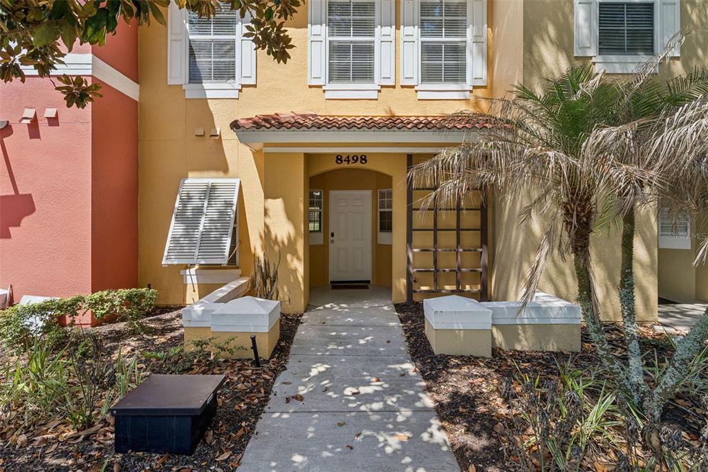 A yellow stucco townhouse exterior features a white front door and a concrete walkway — 8498 CRYSTAL COVE LOOP, KISSIMMEE, FL