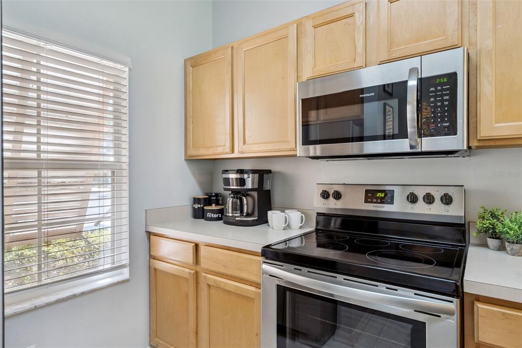 A kitchen features light wood cabinets, stainless steel appliances, and a window with blinds — 8498 CRYSTAL COVE LOOP, KISSIMMEE, FL