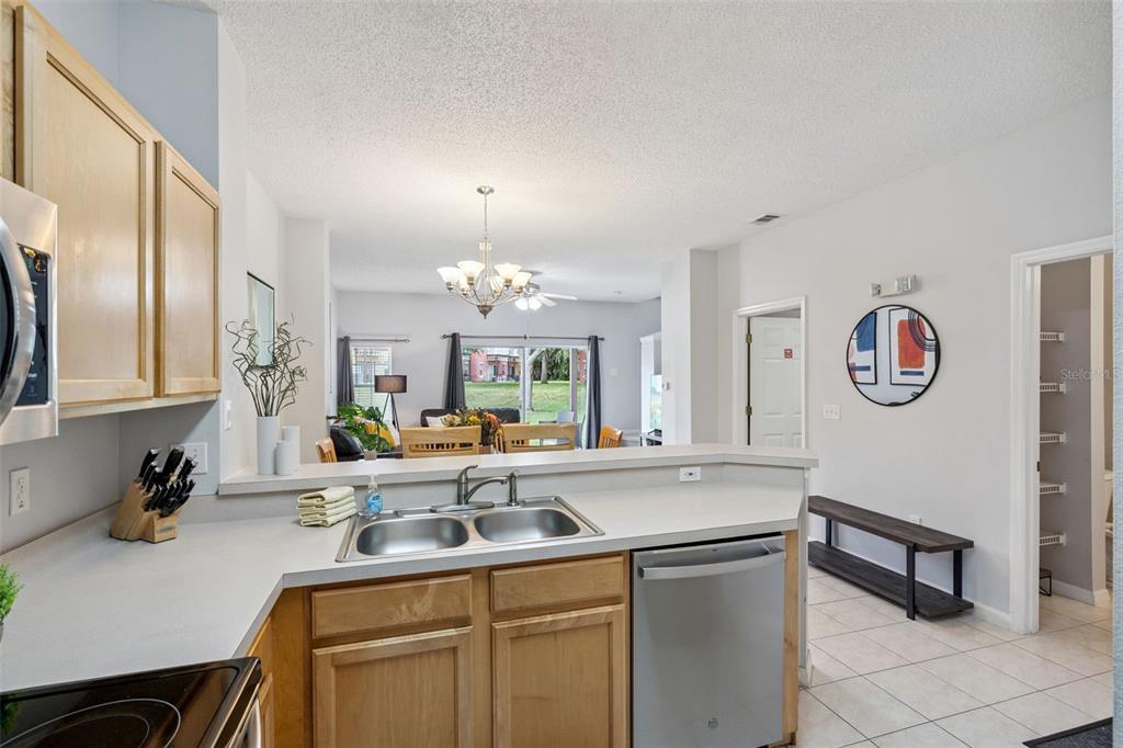 A kitchen with light wood cabinets and a stainless steel dishwasher overlooks a living area — 8498 CRYSTAL COVE LOOP, KISSIMMEE, FL
