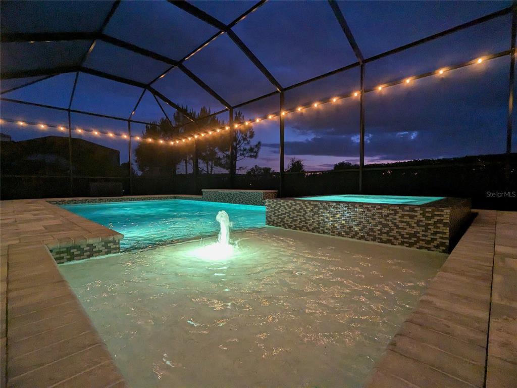 An illuminated swimming pool and hot tub are enclosed within a screened-in patio at night — 4645 ANTRIM DRIVE, SARASOTA, FL