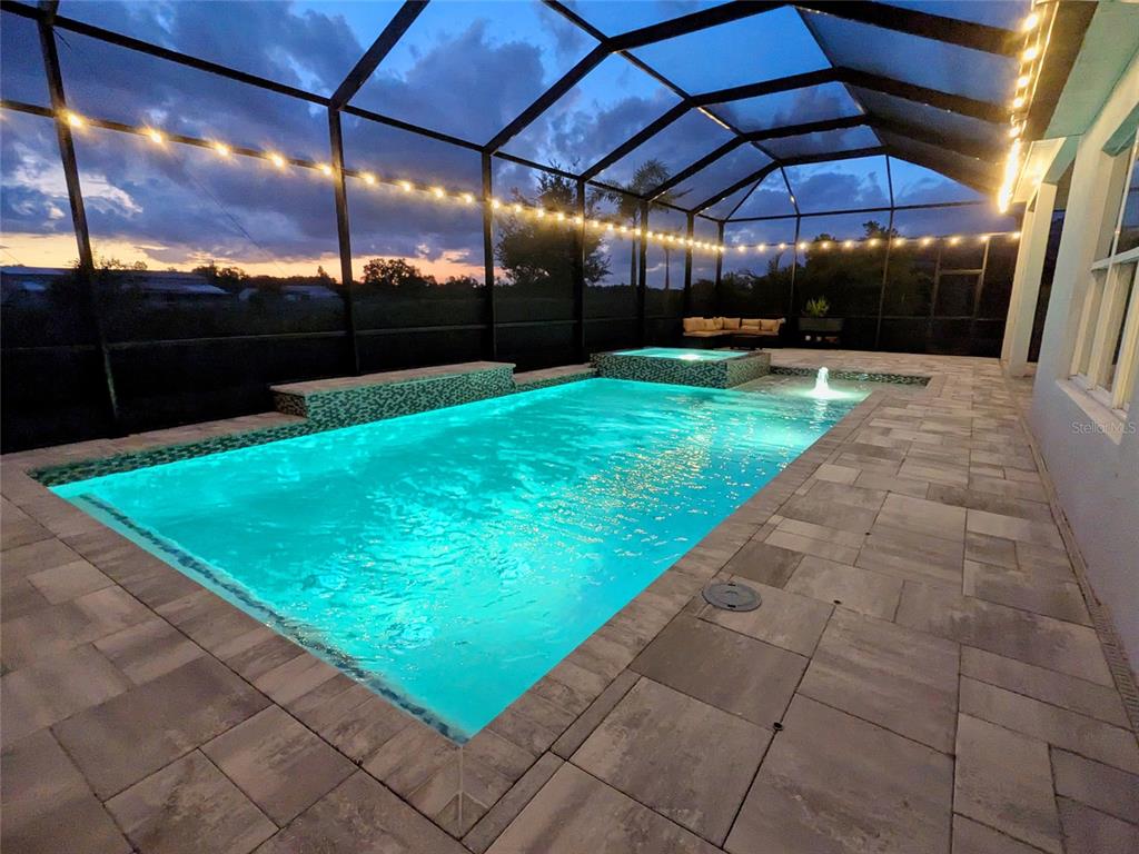 An illuminated rectangular swimming pool and spa are enclosed within a screened-in patio area — 4645 ANTRIM DRIVE, SARASOTA, FL