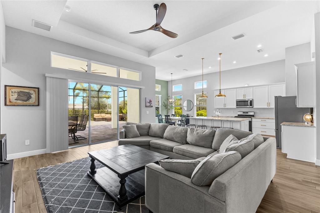 An open-concept living room with a gray sectional sofa, wood floors, and a modern kitchen — 4645 ANTRIM DRIVE, SARASOTA, FL