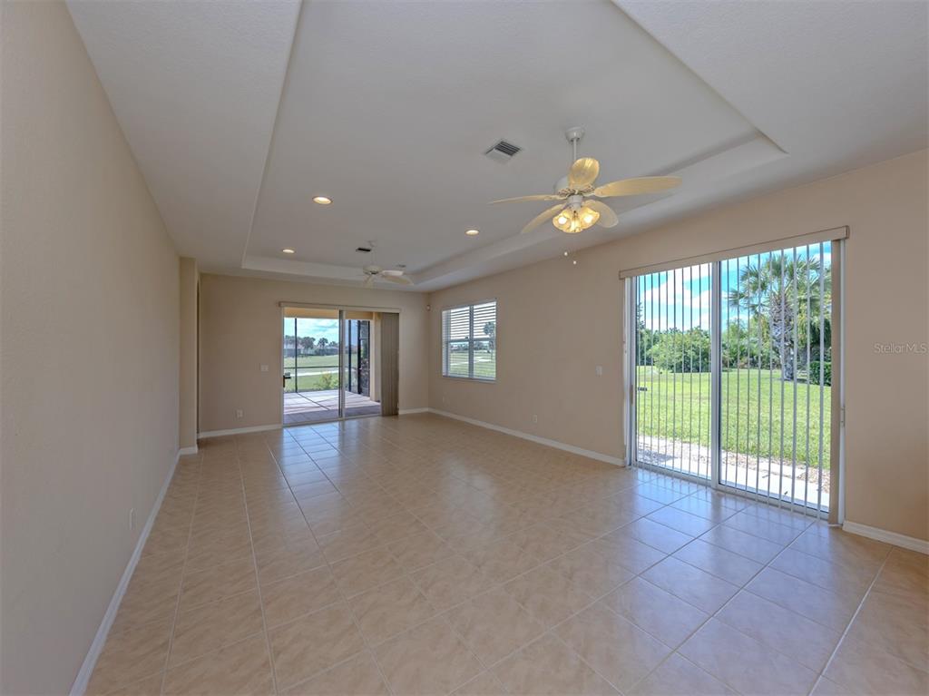 An empty living room features tile flooring, a tray ceiling with fans, and sliding glass doors — 101 MESTRE PLACE, NORTH VENICE, FL